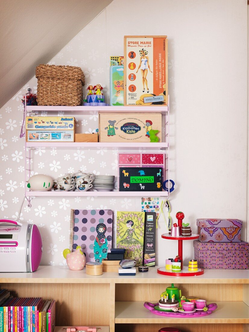 Pink String shelves holding doll's tea set and various toys above open-fronted shelving unit