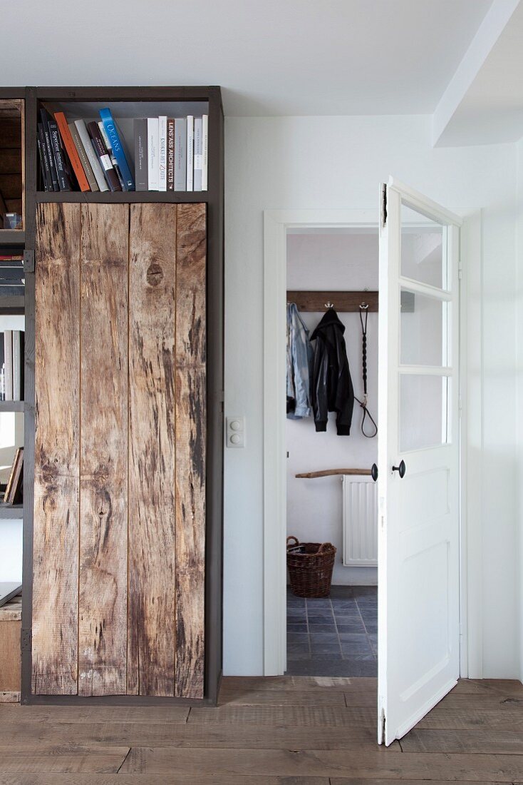 DIY shelving elements with rustic board front next to open door with view of coat hooks in hallway