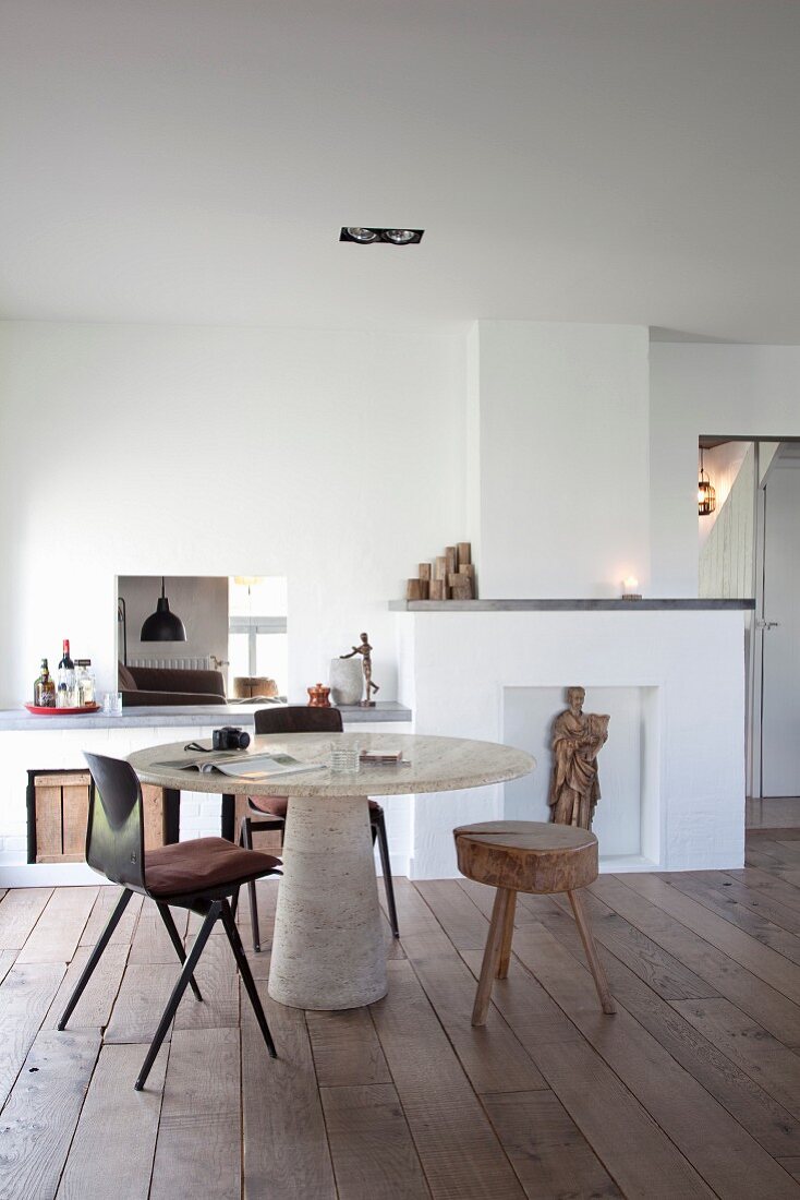 Purist interior with board floor, masonry niches, round table with conical concrete pedestal and 3-legged stool with tree-trunk seat