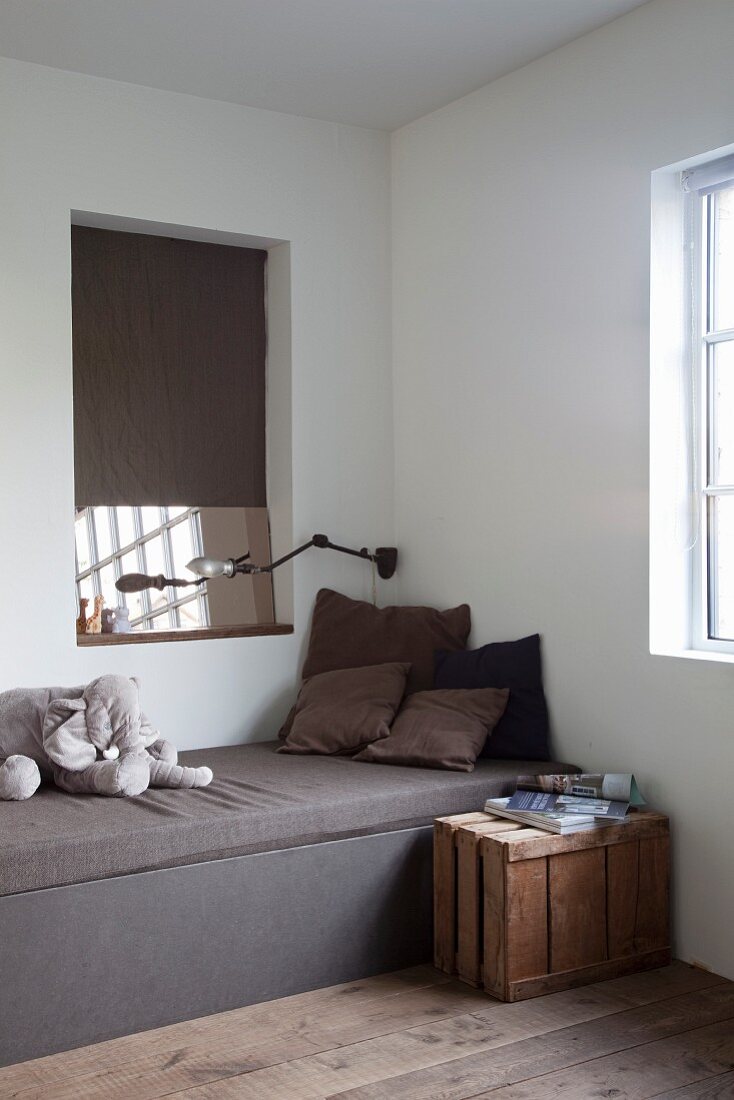 Plüschelefant auf puristischem Kastenbett, darüber eine Wandnische mit Spiegel und Holzkiste als Nachttisch