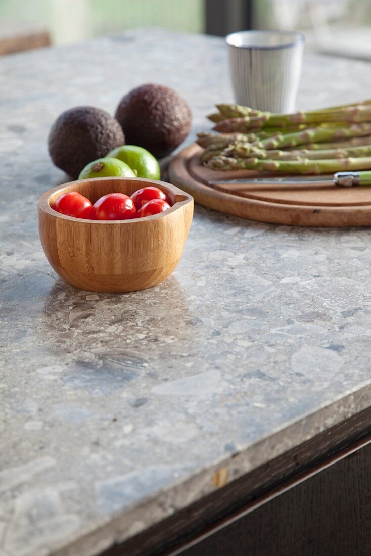 Wooden bowl and chopping board with vegetables on stone worksurface