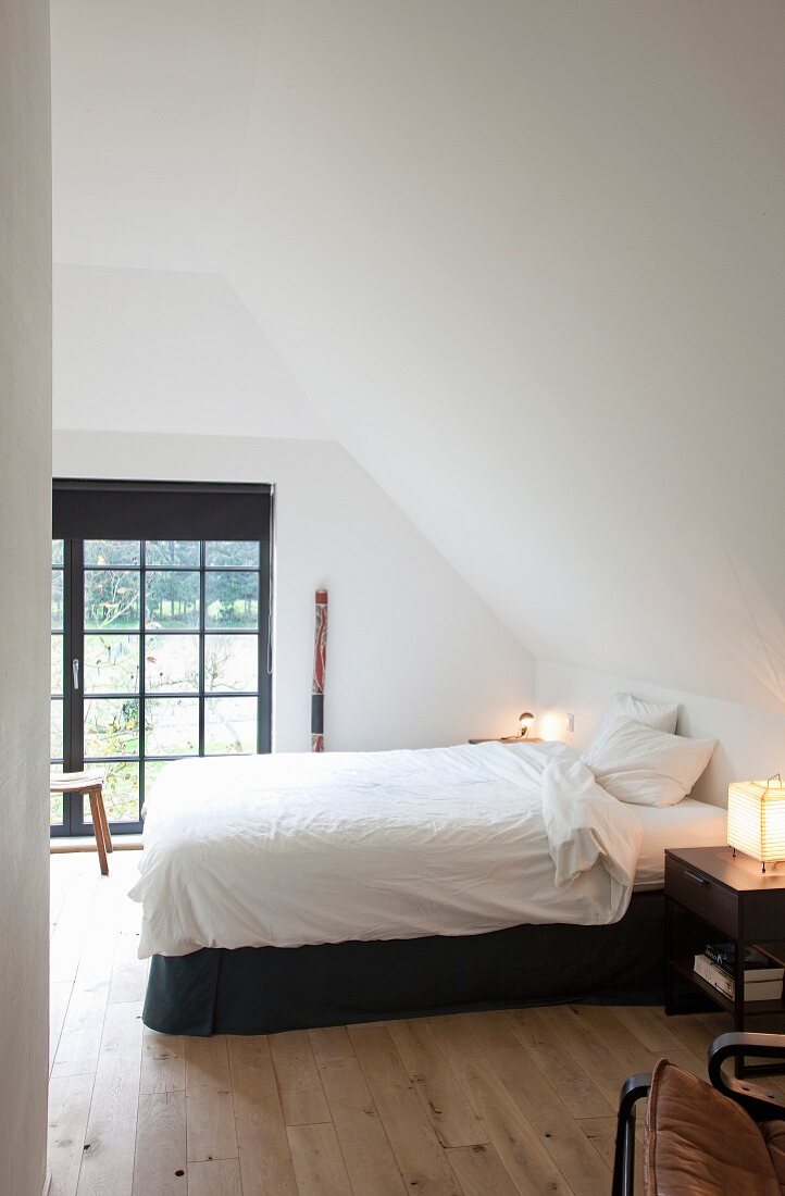 Double bed with white bed linen in bedroom with sloping ceiling and lattice window