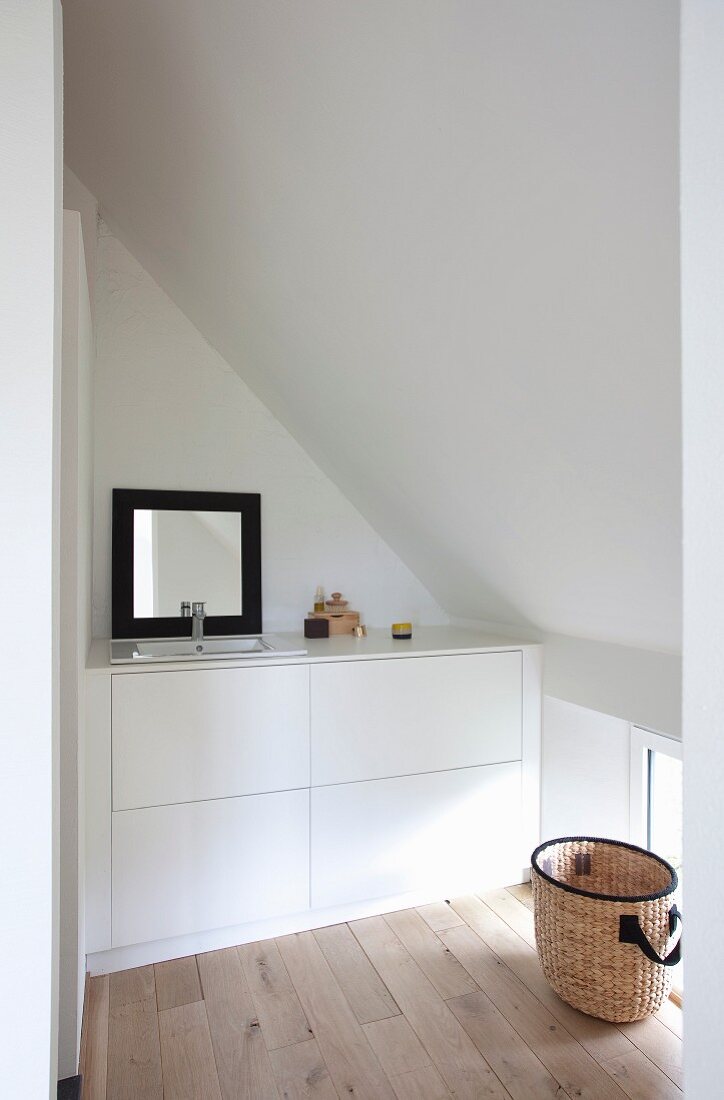 Minimalist fitted washstand below black-framed mirror below sloping ceiling