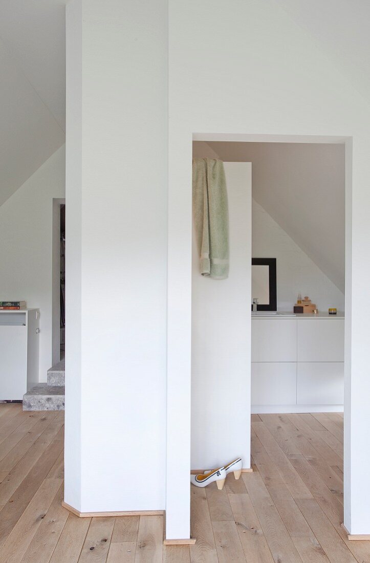 White installations and pale wooden floor in attic bedroom with ensuite bathroom
