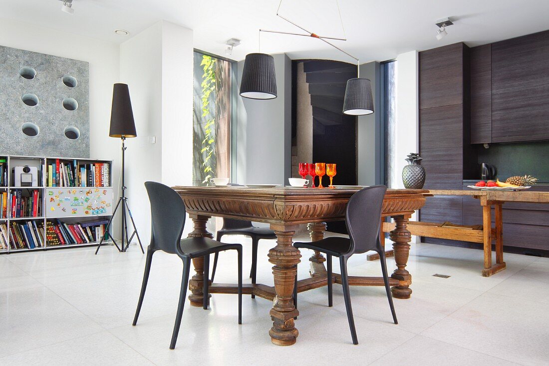 Kitchen-dining area with antique table, plastic chairs, charcoal kitchen counter, open-fronted shelves and standard lamp