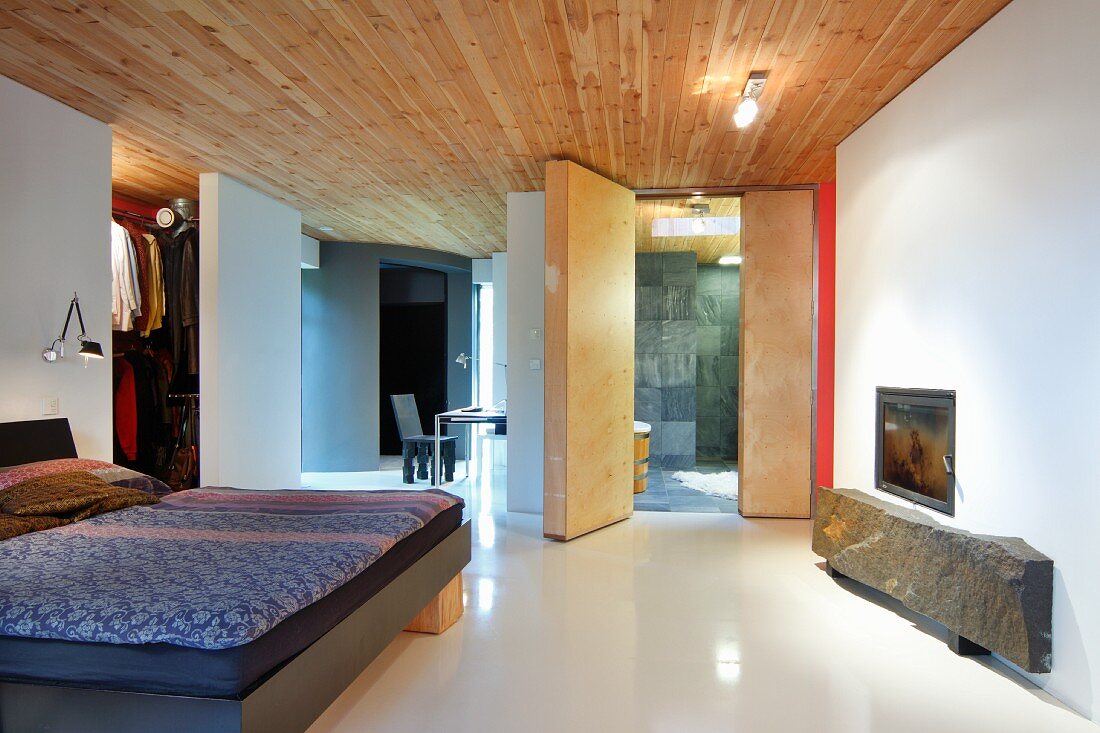 Purist bedroom in modern building: rustic stone slab under glass-fronted fireplace