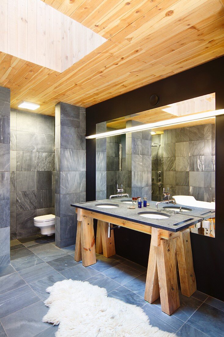 Designer bathroom with washstand on rustic wooden trestles, grey tiles and skylight shaft in wooden ceiling