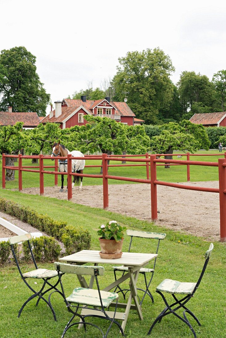 Gartentisch- und stühle auf Rasenfläche, im Hintergrund Pferd auf der Koppel eines Landguts