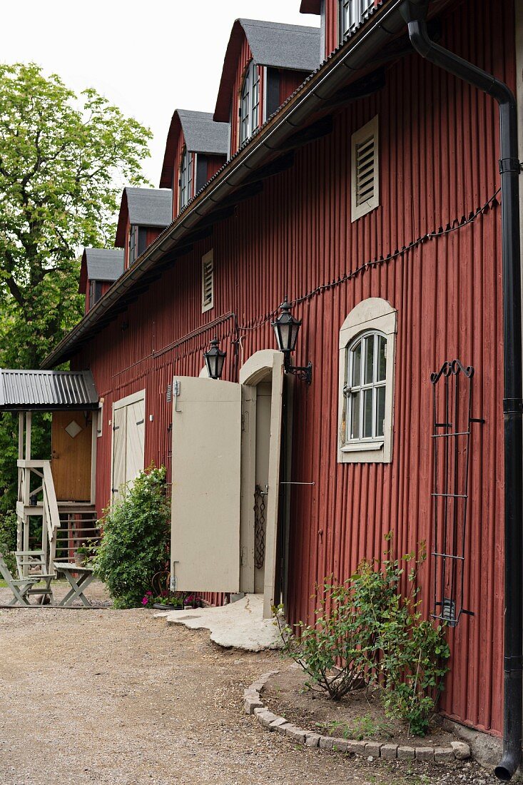 Landhaus mit rotbraun gestrichener Holzwand, vor Fassade kleines Beet