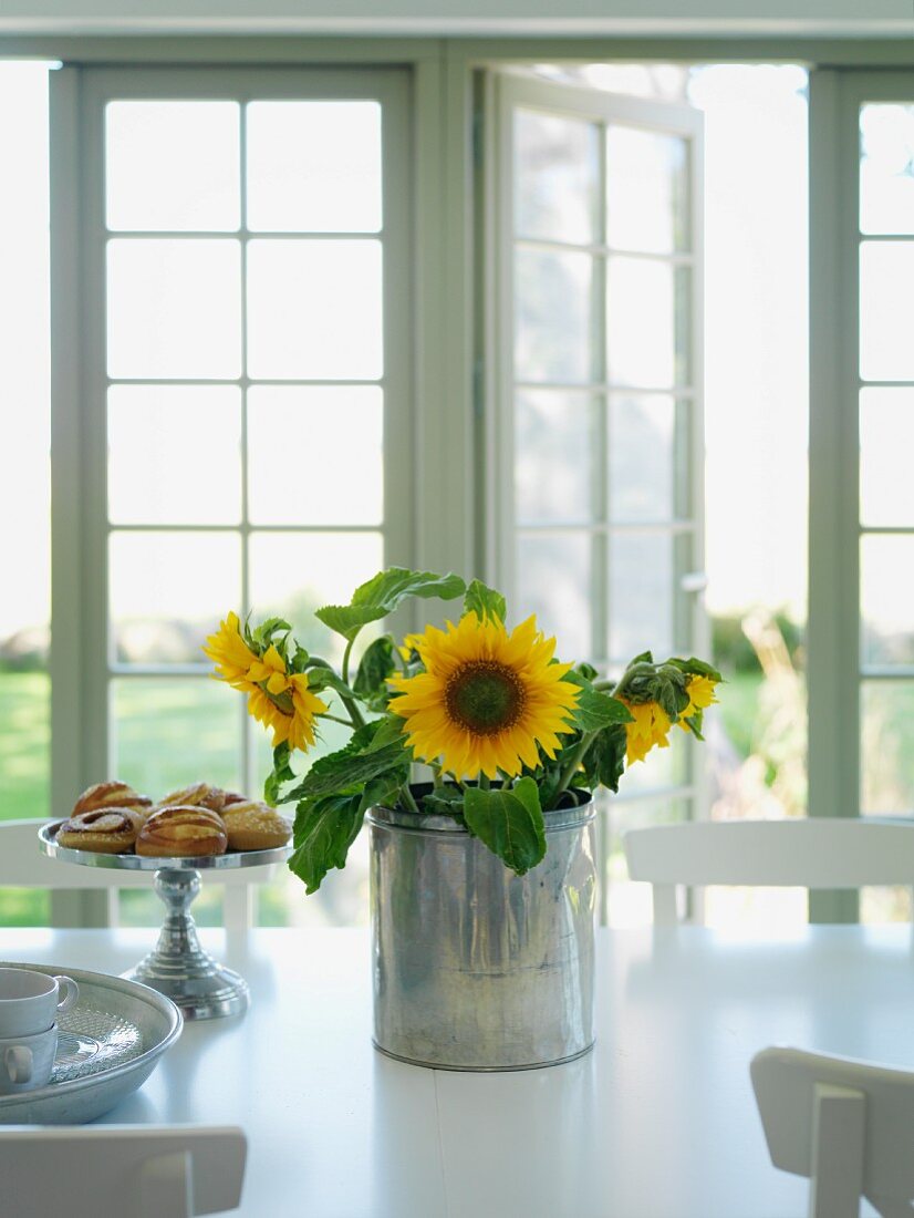 Sonnenblumen in Metall Behälter neben Gebäckständer auf weißem Tisch