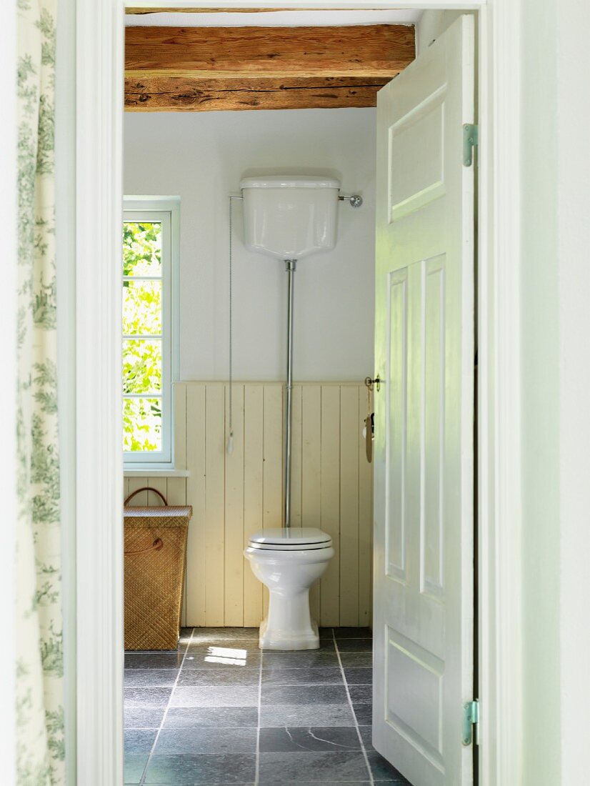 Blick durch offene Tür auf Toilette auf grauem Fliesenboden, in ländlichem Bad