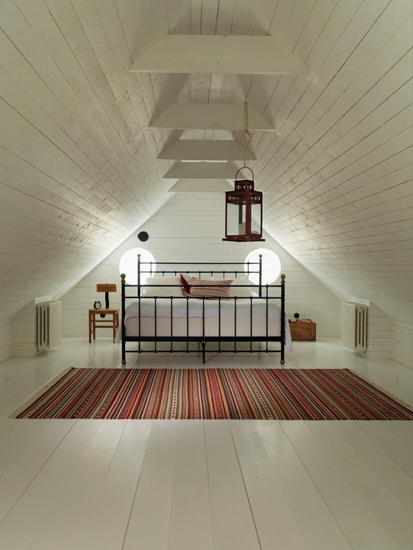 Double bed with black metal frame and striped rug in converted attic with white-painted wood cladding