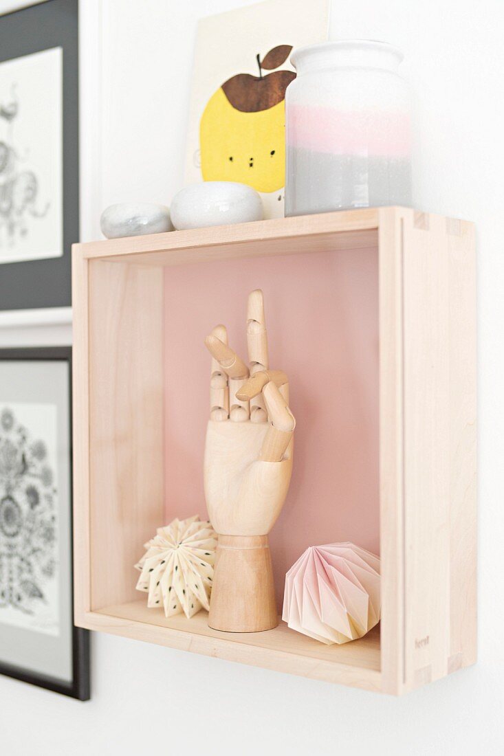Segmented, wooden hand and origami balls in display case hung on wall