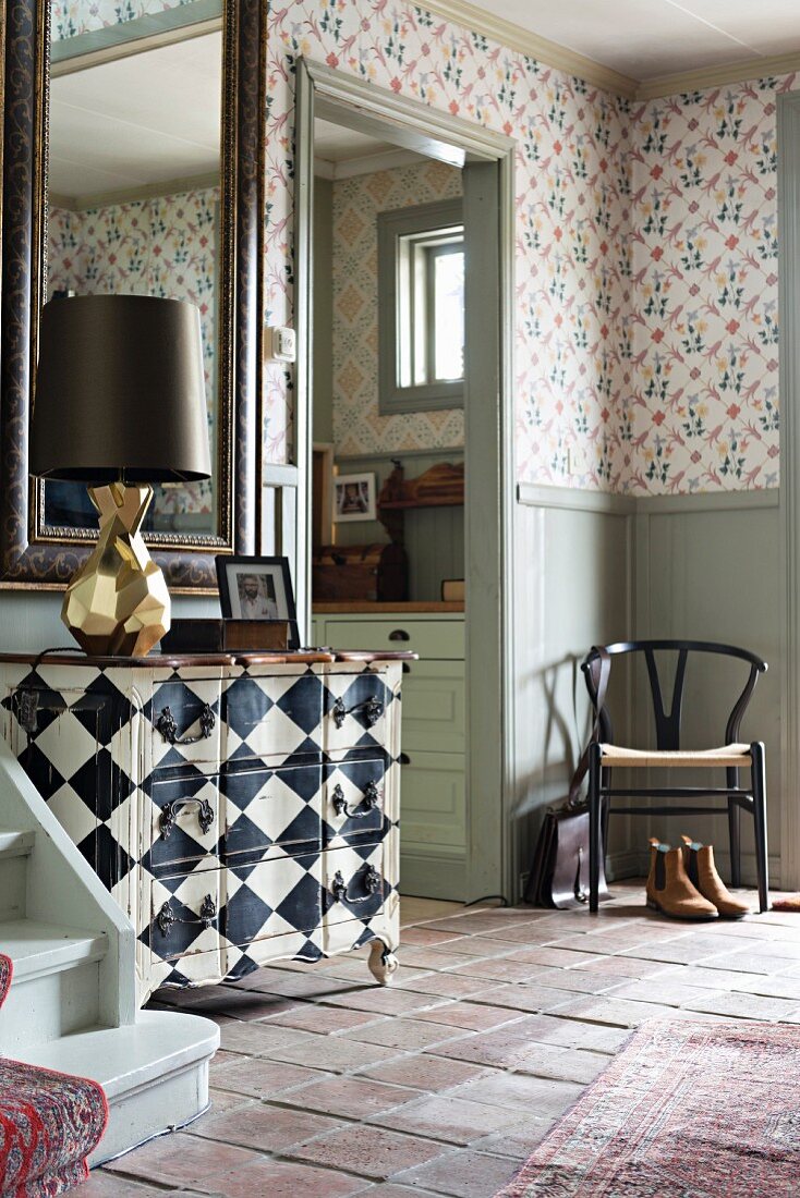 Chequered chest of drawers in rustic foyer with Tessin wallpaper design and classic chair in corner