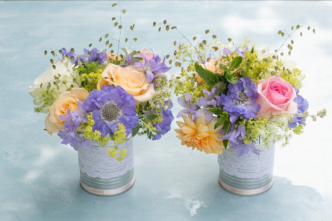 Two posies of roses and scabious in decorative tins