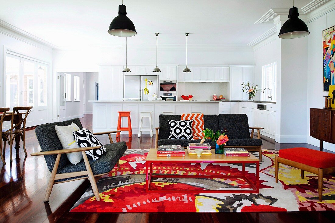 Retro lounge with colourful rug and exotic-wood parquet floor in open-plan interior with view of white kitchen