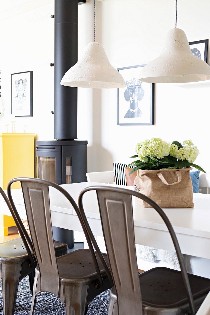 Retro metal chairs at white dining table below pendant lamps with ceramic lampshades