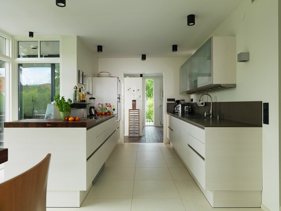 Gegenüberliegende Küchenzeilen in offener Küche mit grossformatigem Fliesenboden, im Hintergrund Durchgang mit Blick in Eingangsbereich