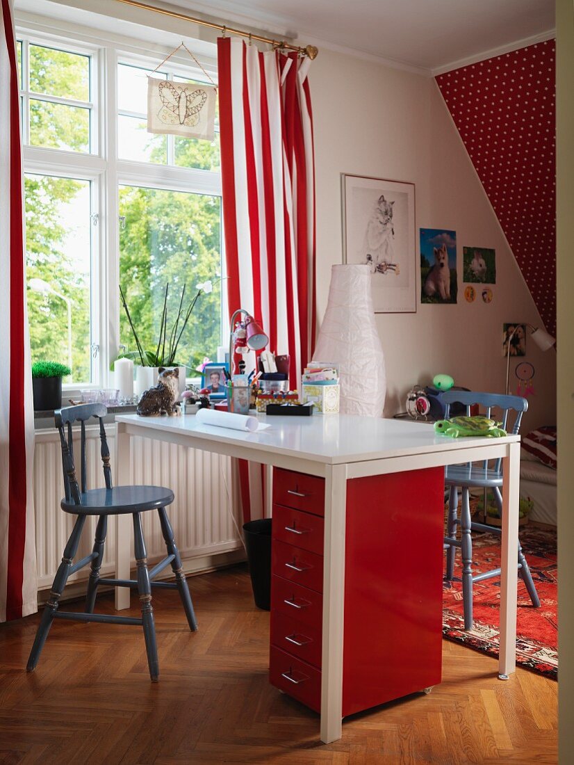 Weisser Schreibtisch darunter roter Schubladencontainer, am Fenster mit rot-weiss gestreiftem Vorhang im Kinderzimmer