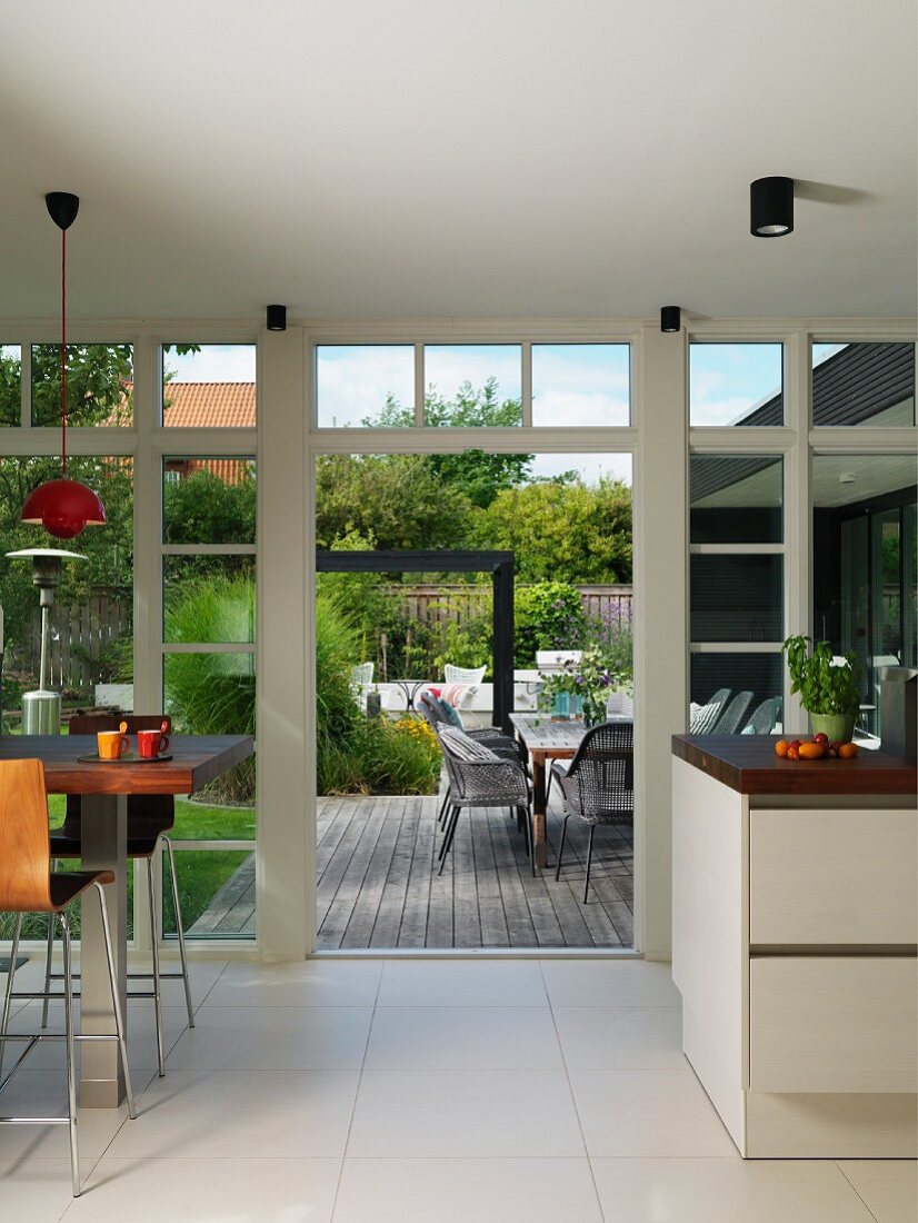 Open-plan kitchen with dining area next to glass wall, open terrace doors and view of outdoor seating area