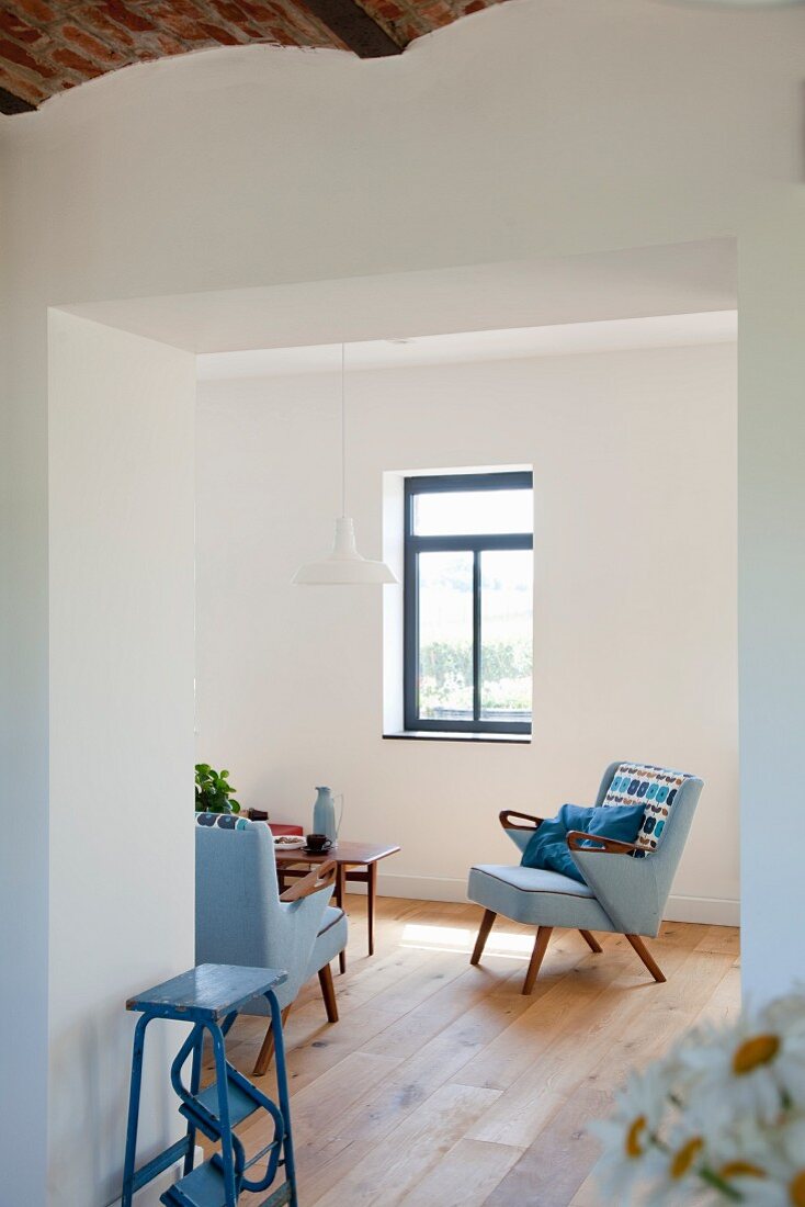 Renovated foyer with open doorway and view of fifties-style armchair with pale blue cover in minimalist interior