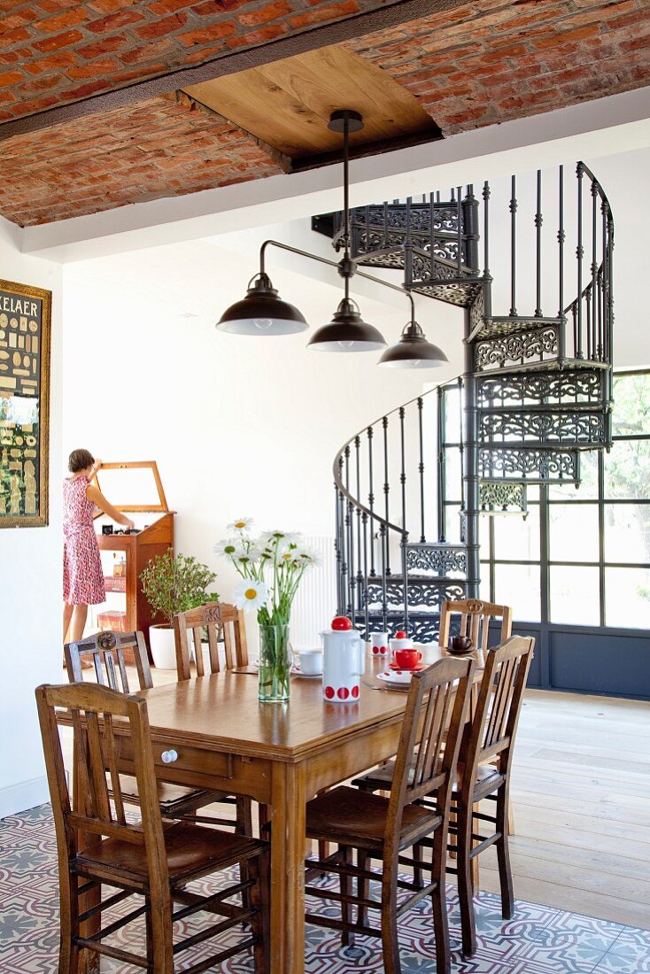 Dining area in front of cast-iron, vintage-style spiral staircase in open-plan interior