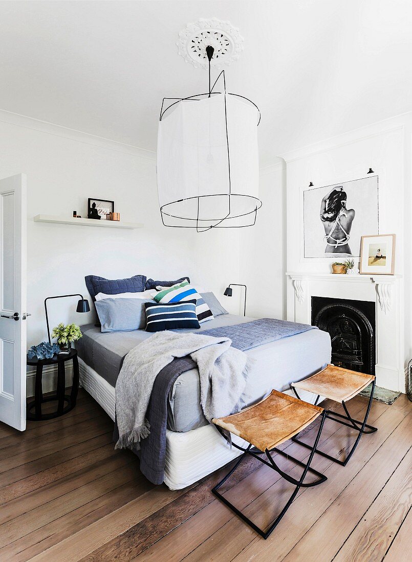Box-spring bed, old open fireplace, leather stools and framed photographic artwork in bright bedroom