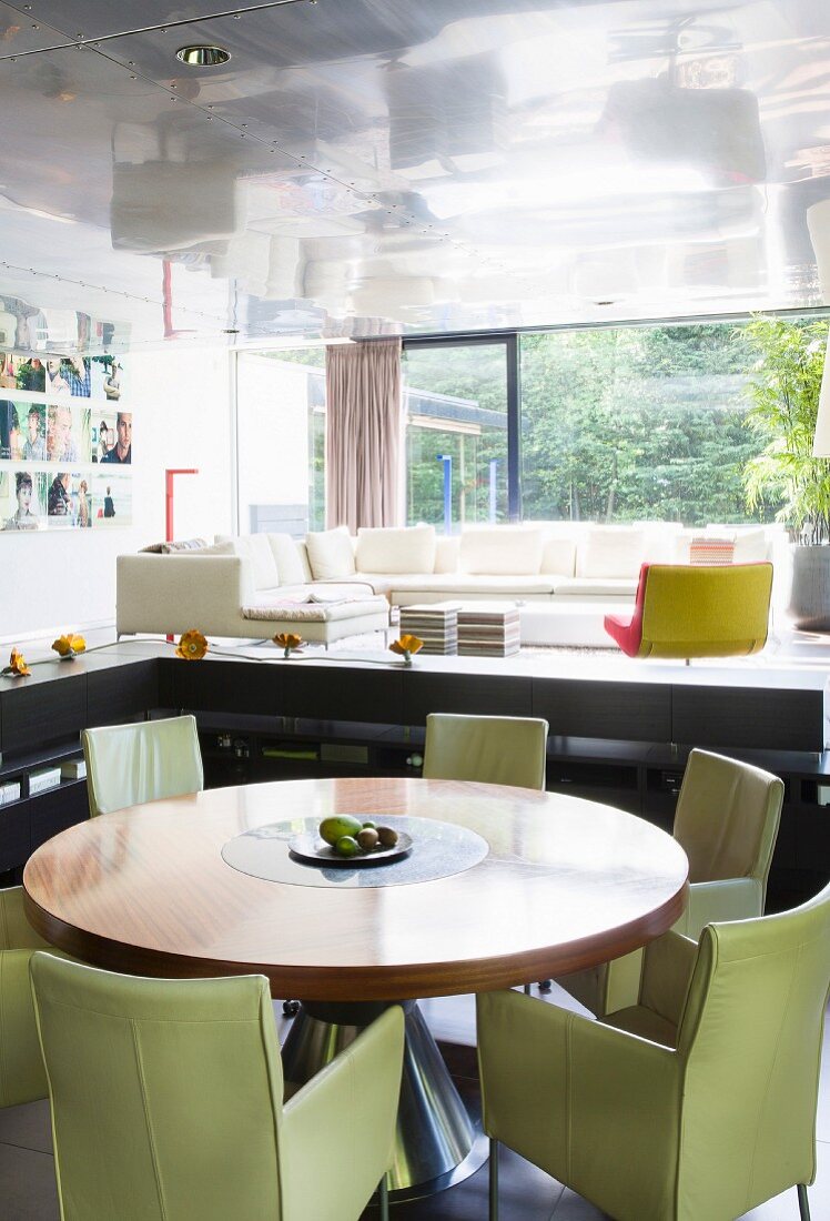 Modern living space with panoramic window in luxury apartment; round dining table and pastel green designer armchairs in foreground