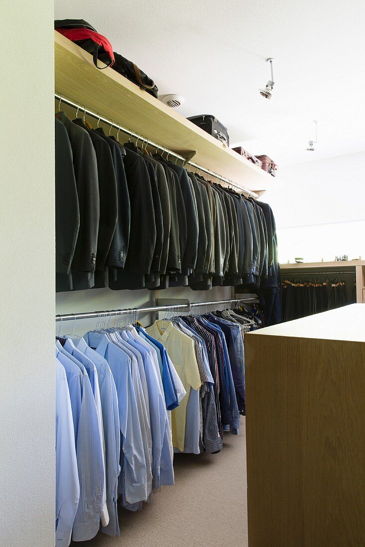 Suit jackets and shirts hanging from clothes rails in walk-in wardrobe
