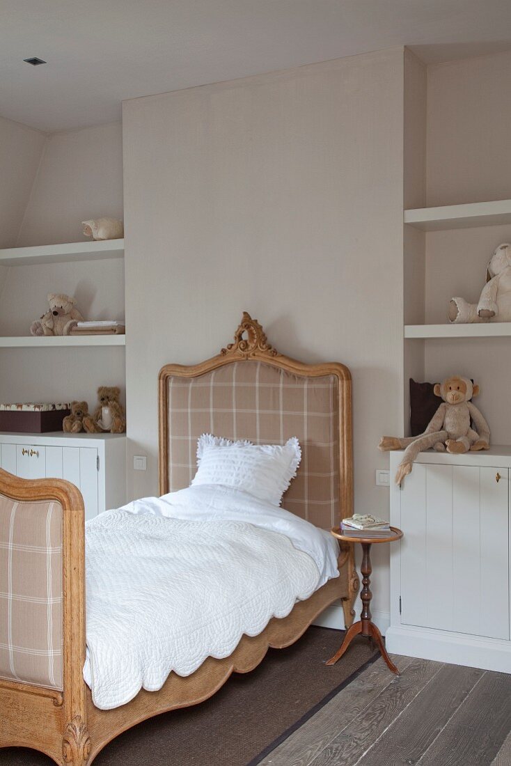 Antique sleigh bed with carved wooden frame and white bed linen flanked by fitted shelves and cabinets in niches