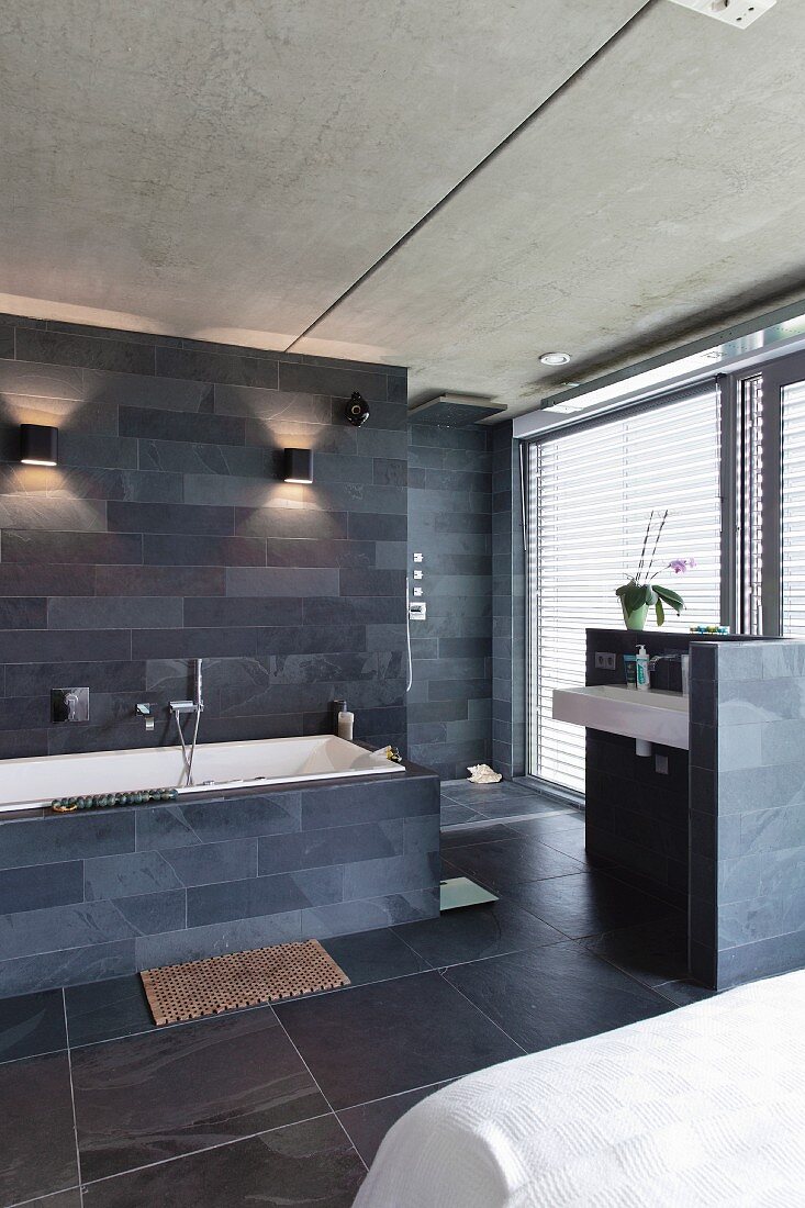 Designer bathroom area with slate tiles on walls and floor in open-plan bedroom