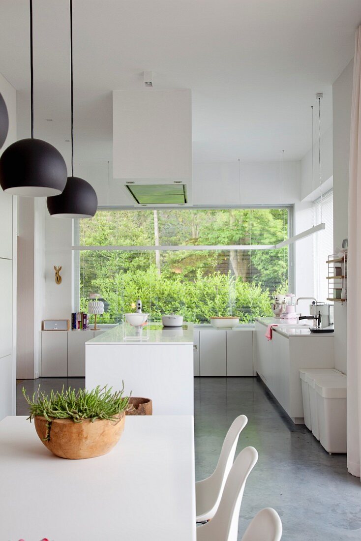 White, open-plan kitchen with large window overlooking garden; dining table and shell chairs in foreground