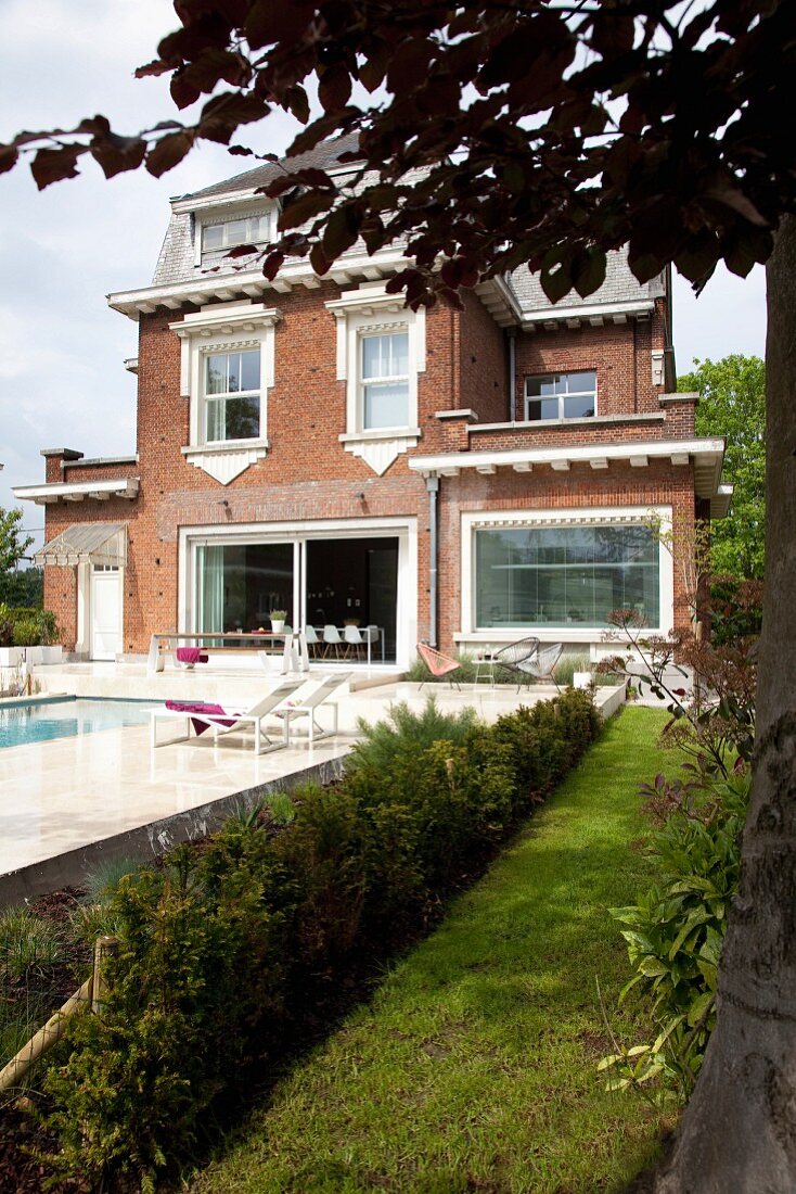 Pool and sun terrace outside traditional Belgian brick house with decorative white elements and large modern windows