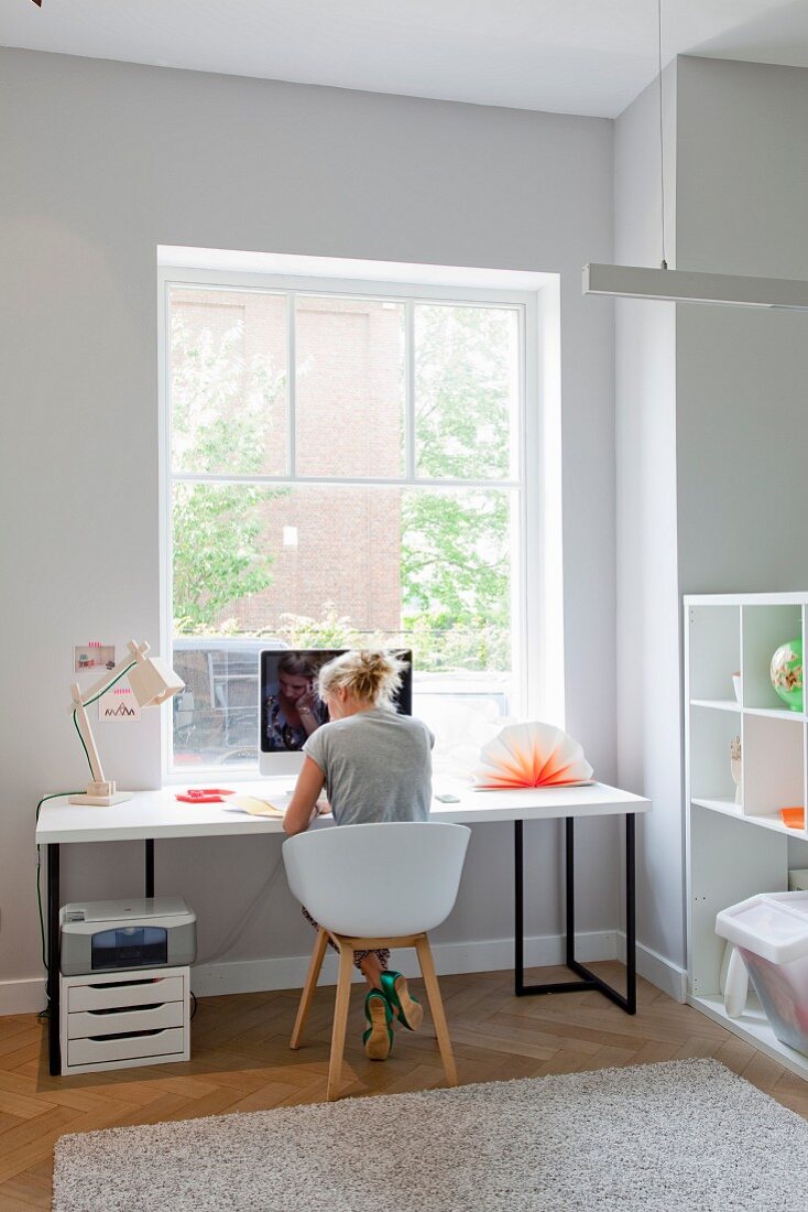 Bright, modern study with woman sitting on shell chair at desk below window