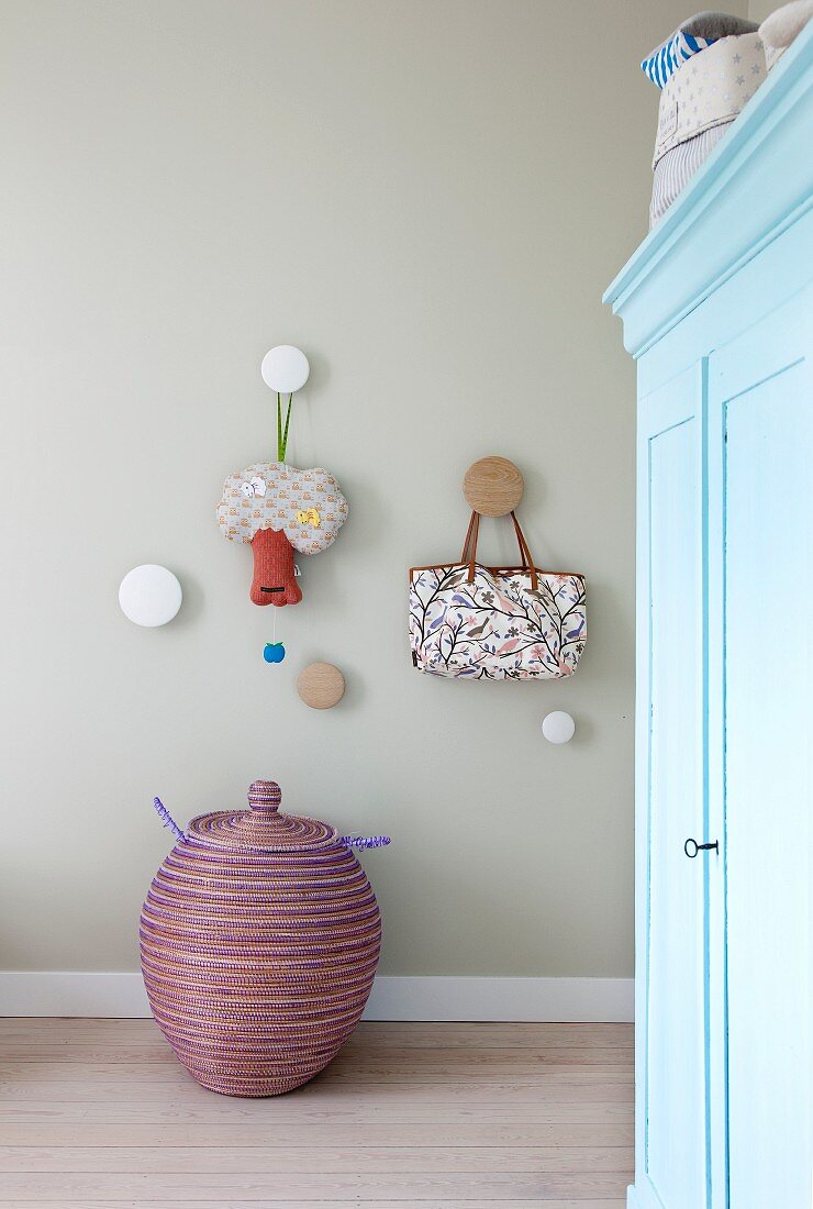 Round pegs on wall above lidded basket; light blue vintage wardrobe in foreground
