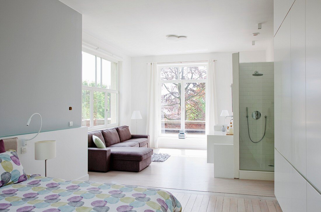 View from open-plan bedroom to sofa and shower in light-flooded ensuite bathroom