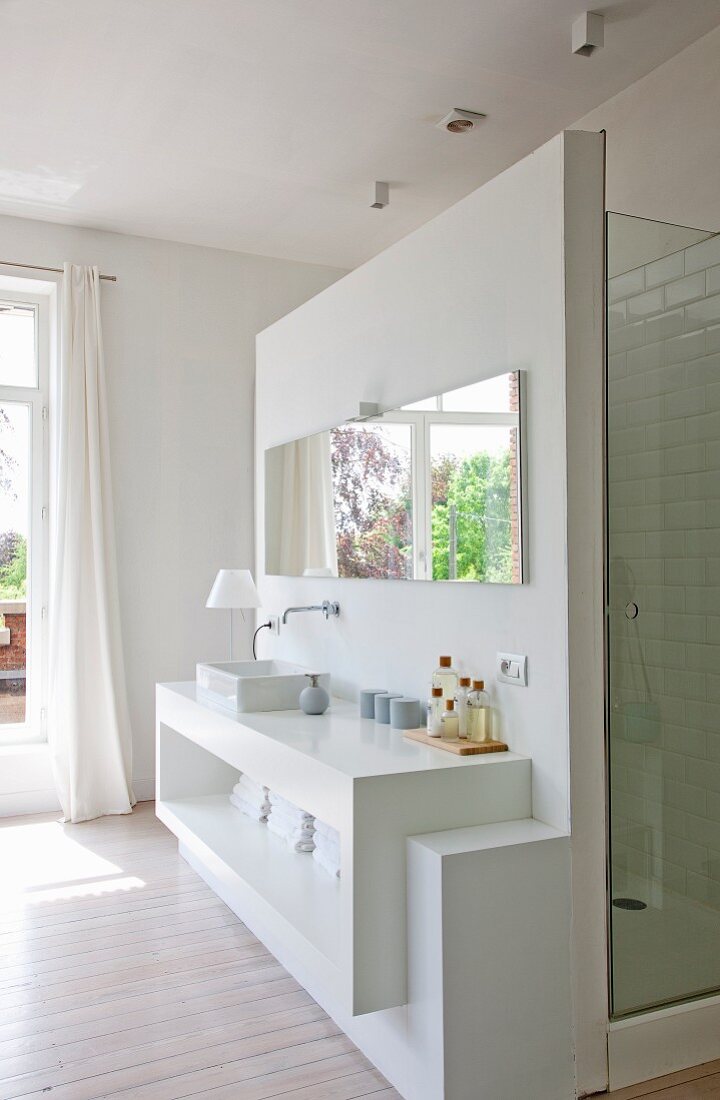 Cubic washstand with shelf and mirror on wall screening shower cubicle in open-plan ensuite bathroom
