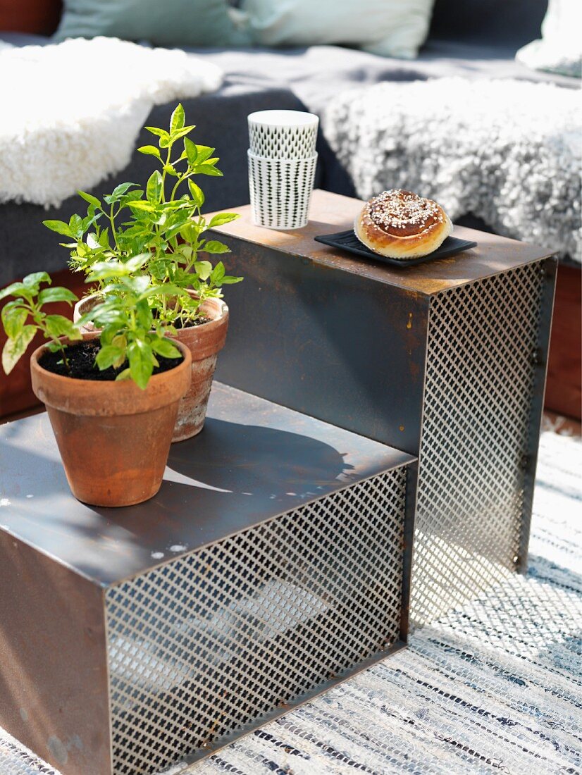 Potted herbs and pastries on set of rusty metal and mesh side tables