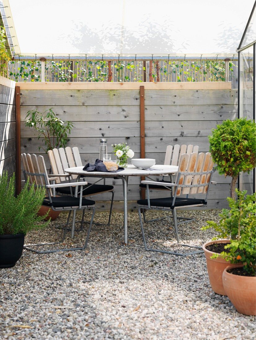 Sitzplatz auf kleiner, gekiester Terrassenfläche unter gespanntem Sonnensegel mit Holzrahmen