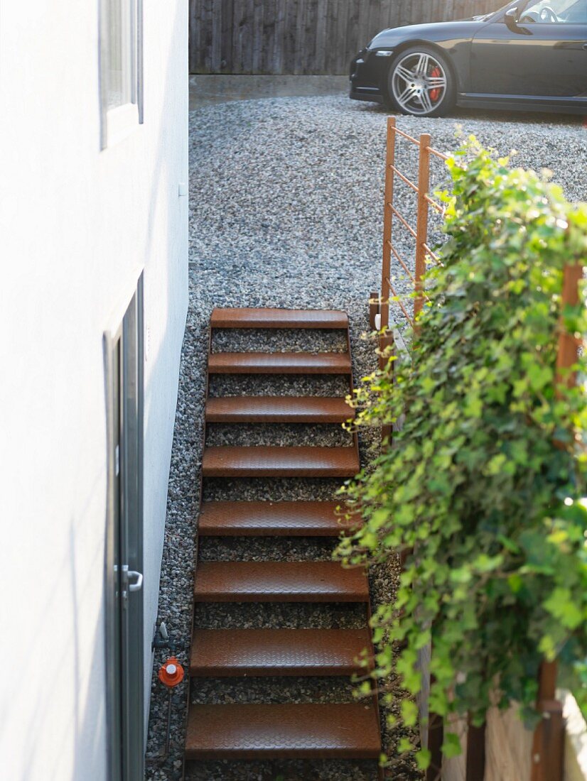 Minimalist external staircase with rusty metal treads; car on gravel drive in background