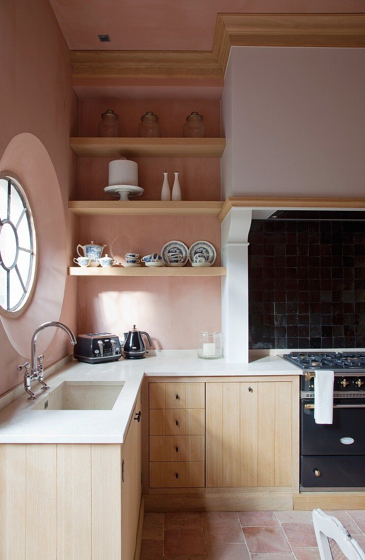 Schlichte Küche mit Holzfronten an Unterschränken, vor rosa Wand