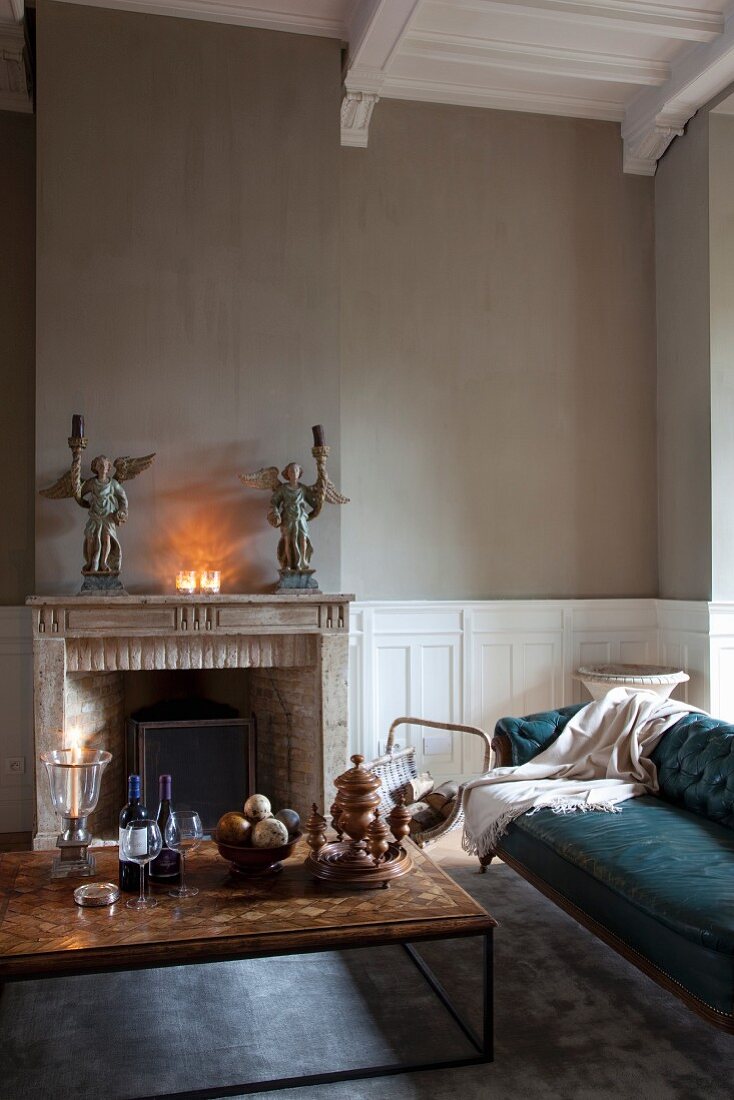 Coffee table and antique sofa in front of fireplace and angel candlesticks on mantelpiece in renovated interior