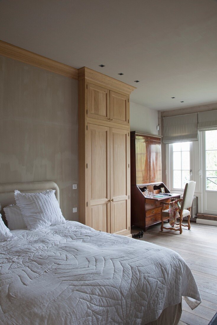 Double bed, fitted wardrobe with carved doors and antique bureau in background