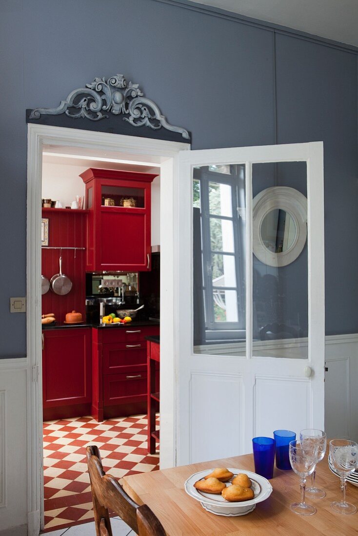 Dining table in front of open door and view of red-painted cabinets in kitchen