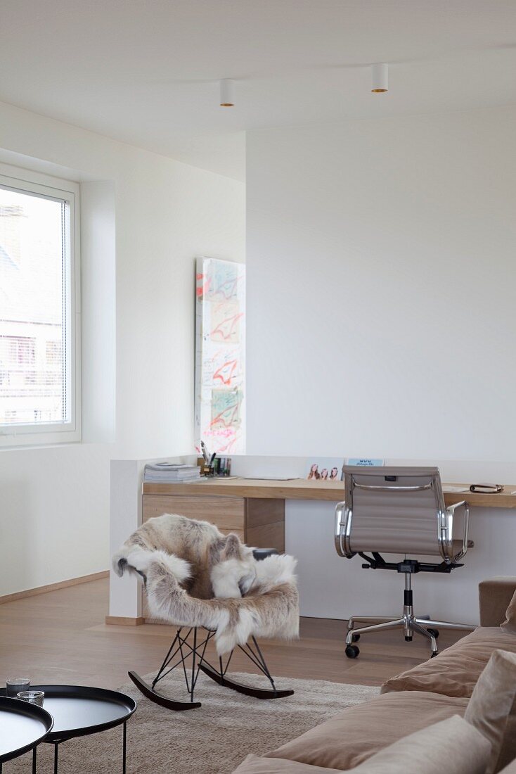 Maßgefertigter moderner Holzschreibtisch mit Klassiker Bürostuhl im gemütlichen Loungebereich mit Eames-Schaukelstuhl und Tierfell