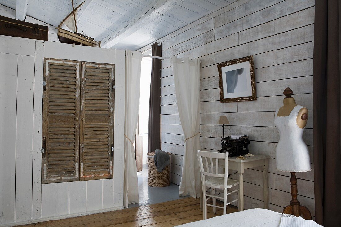 Einbauschrank mit Holzlamellentüren als Raumteiler, seitlich an Wand kleiner Schreibtisch neben Vintage Schneiderpuppe in ländlichem Schlafzimmer