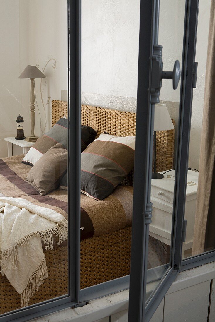 Blick durch geöffnetes Innenfenster auf Bett mit Bettwäsche in Streifenoptik und verschiedene Brauntöne