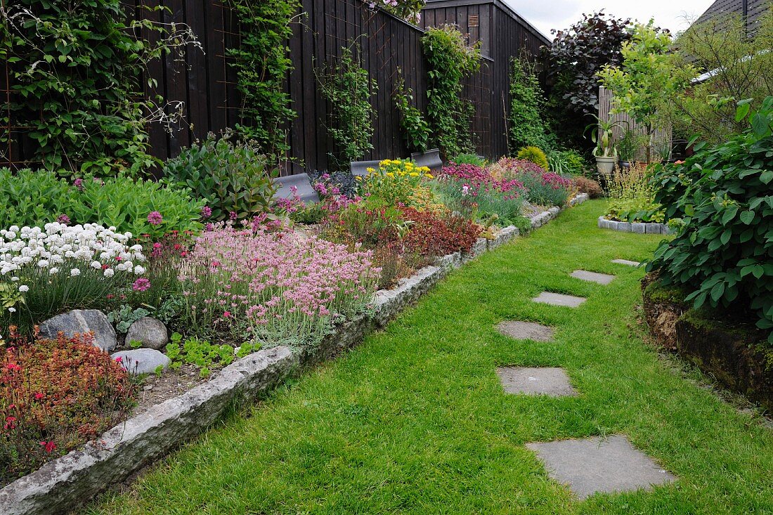 Flowering plants in bed with stone surround and stepping stones in clipped lawn in garden