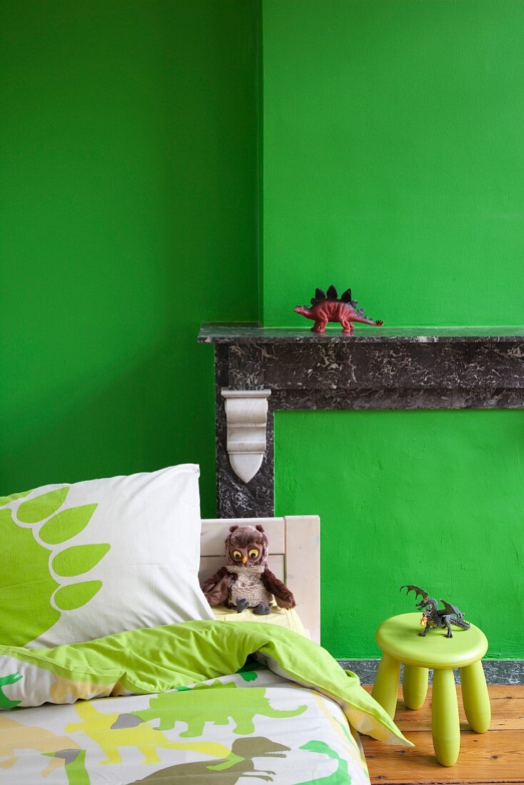 Bed in front of mantelpiece of disused fireplace in child's bedroom with green wall