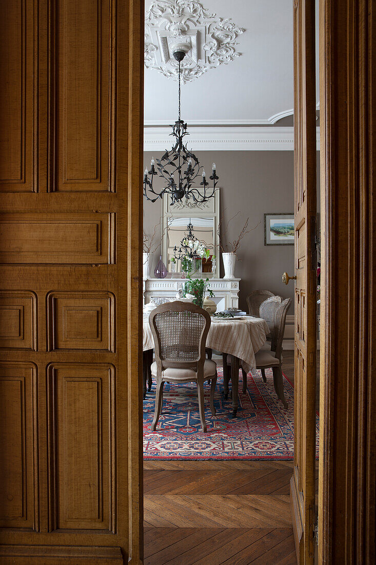 View of chairs and table under chandelier in grand dining room seen though open double doors